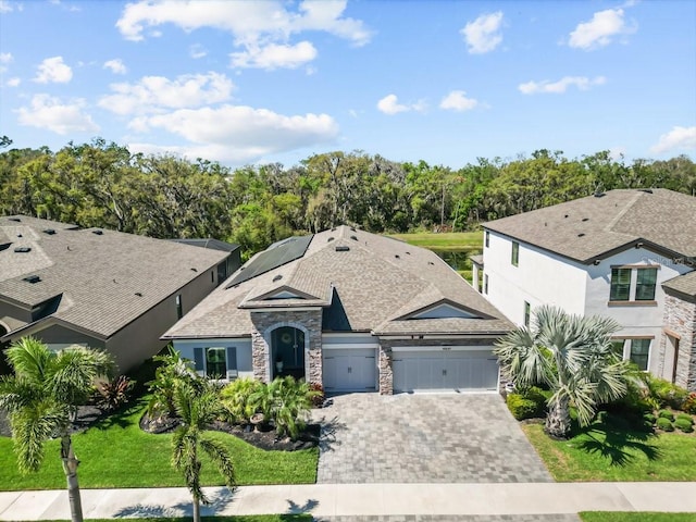 view of front of home with a front yard, stucco siding, a garage, stone siding, and decorative driveway