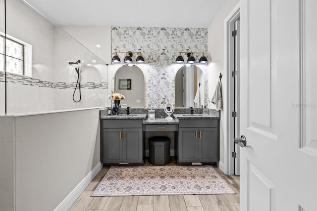 bathroom featuring vanity, wood finished floors, baseboards, and a walk in shower