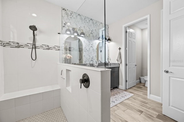 bathroom with baseboards, walk in shower, toilet, wood finished floors, and vanity