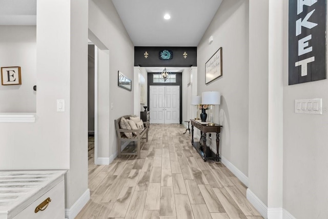 foyer featuring baseboards, light wood-style floors, and a chandelier