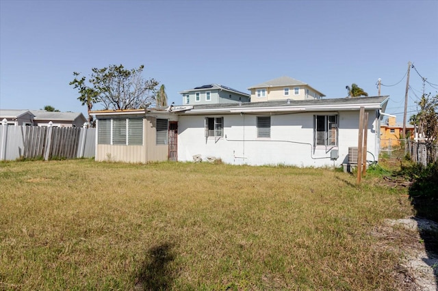 rear view of house with concrete block siding, a lawn, and fence