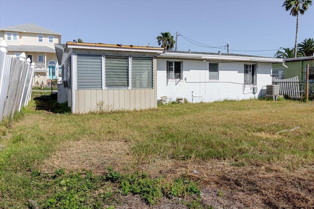 rear view of property featuring concrete block siding, a yard, fence, and central AC