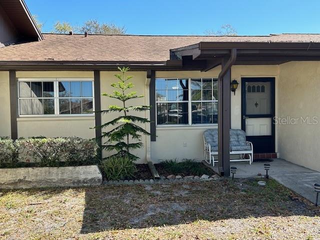 property entrance with a shingled roof and stucco siding