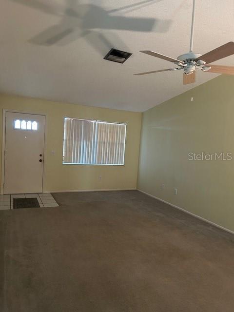 interior space with visible vents, ceiling fan, baseboards, lofted ceiling, and carpet flooring