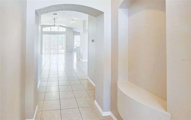 hall featuring lofted ceiling, light tile patterned flooring, arched walkways, and baseboards