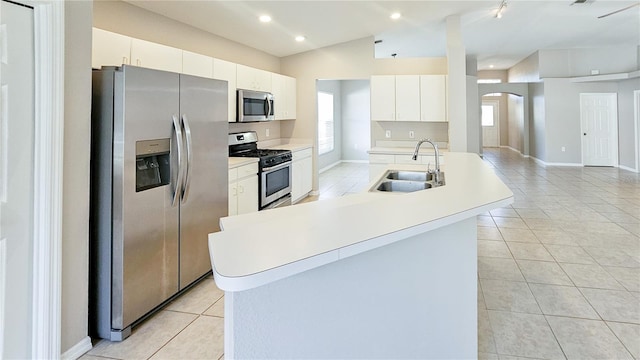 kitchen featuring light tile patterned flooring, an island with sink, arched walkways, a sink, and appliances with stainless steel finishes