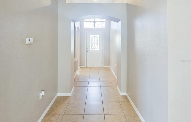 doorway to outside with light tile patterned floors, baseboards, and arched walkways