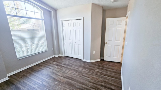 unfurnished bedroom with dark wood finished floors, baseboards, a closet, and a textured ceiling