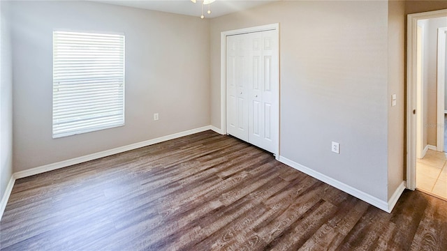 unfurnished bedroom featuring a closet, baseboards, and dark wood finished floors