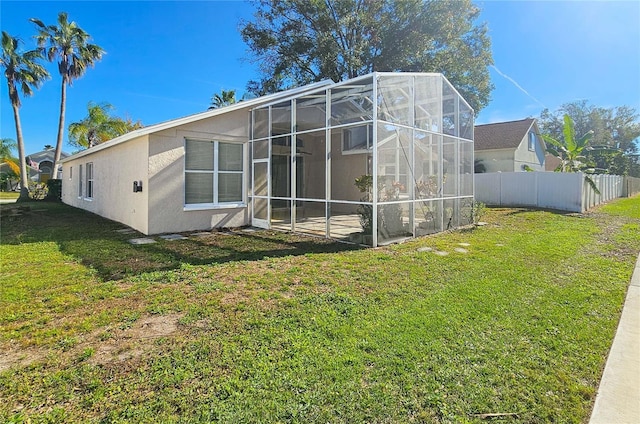 back of property with a lanai, stucco siding, a lawn, and fence