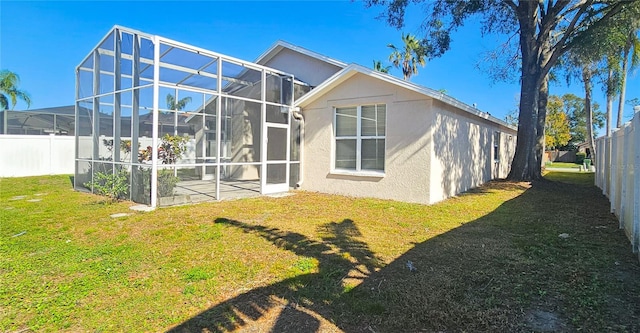 rear view of property with stucco siding, a yard, a lanai, and fence