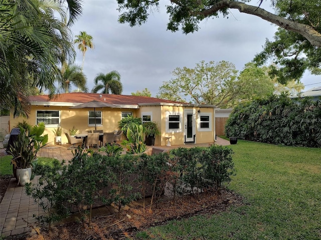 rear view of house featuring a lawn, fence, stucco siding, and a patio area