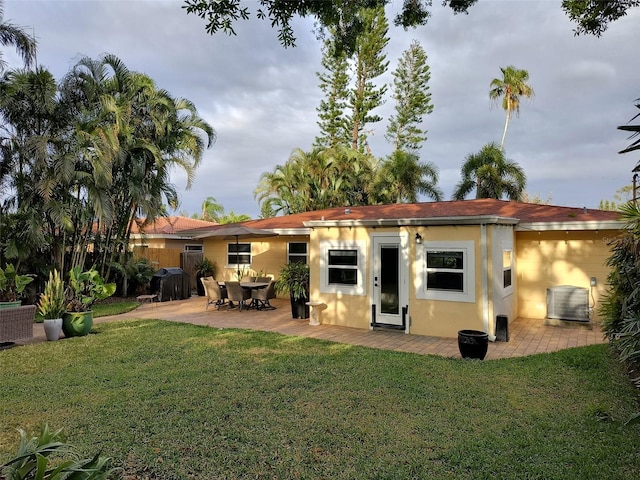 rear view of house with central air condition unit, stucco siding, a patio area, and a yard