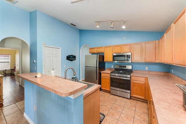 kitchen featuring light tile patterned floors, light brown cabinets, arched walkways, stainless steel appliances, and light countertops