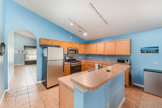 kitchen featuring light brown cabinetry, a sink, arched walkways, appliances with stainless steel finishes, and light tile patterned floors