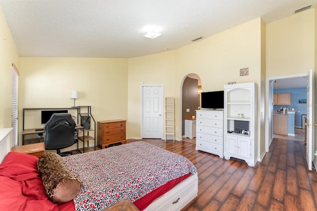 bedroom featuring visible vents, high vaulted ceiling, wood finished floors, arched walkways, and baseboards