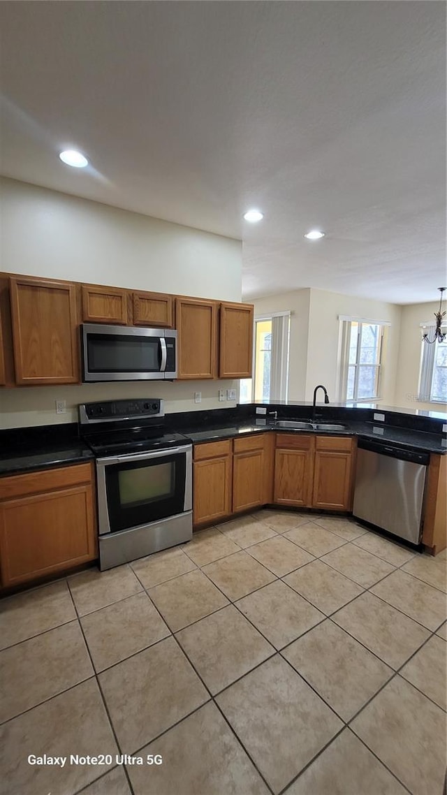 kitchen with a sink, dark countertops, appliances with stainless steel finishes, brown cabinetry, and light tile patterned floors