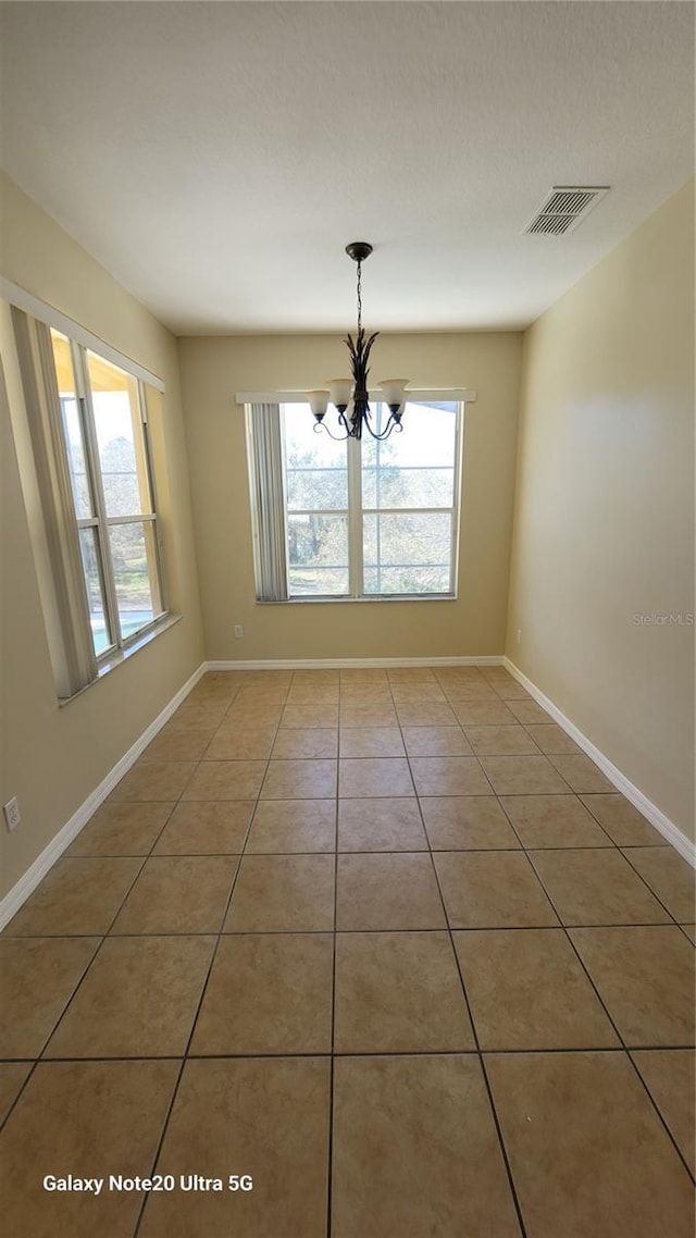 unfurnished room featuring a notable chandelier, visible vents, baseboards, and light tile patterned flooring