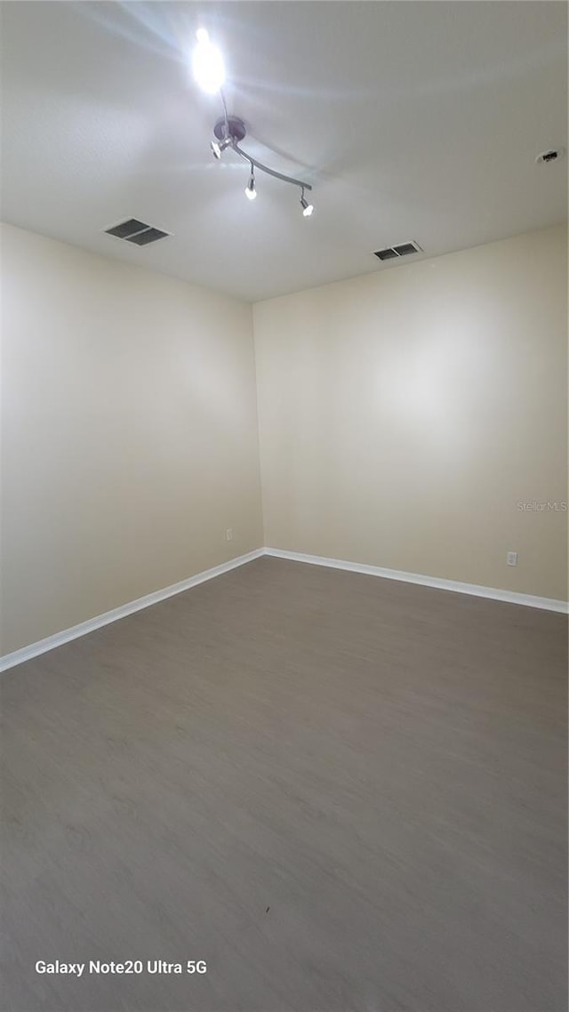 spare room with wood finished floors, visible vents, and baseboards