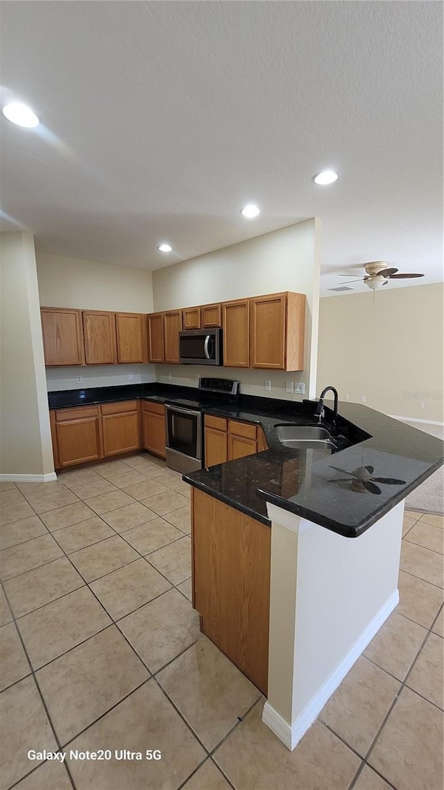 kitchen featuring light tile patterned floors, brown cabinets, appliances with stainless steel finishes, a peninsula, and a sink