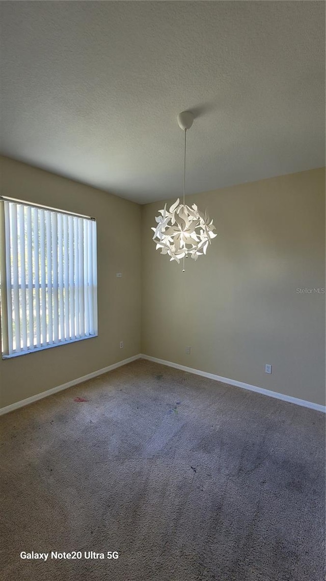 carpeted spare room with a notable chandelier, baseboards, and a textured ceiling