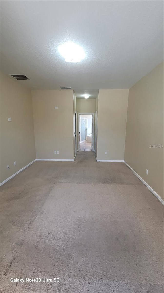 unfurnished room featuring light colored carpet, visible vents, and a textured ceiling