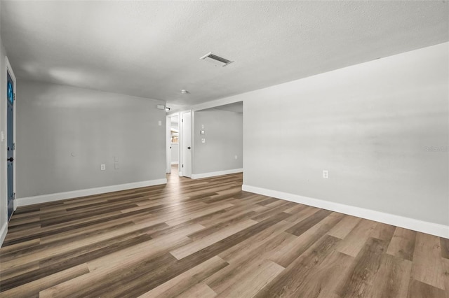 unfurnished room featuring a textured ceiling, wood finished floors, visible vents, and baseboards