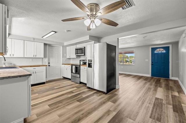 kitchen with light wood-style flooring, appliances with stainless steel finishes, white cabinets, a ceiling fan, and a sink