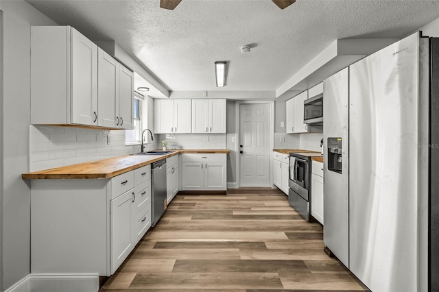 kitchen with light wood finished floors, a sink, stainless steel appliances, wood counters, and tasteful backsplash