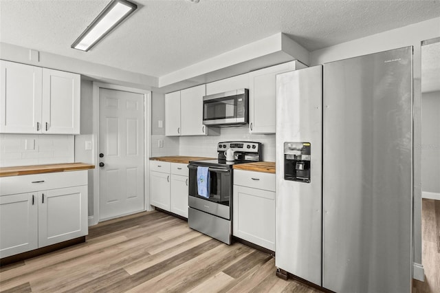 kitchen with light wood finished floors, white cabinets, appliances with stainless steel finishes, and wood counters