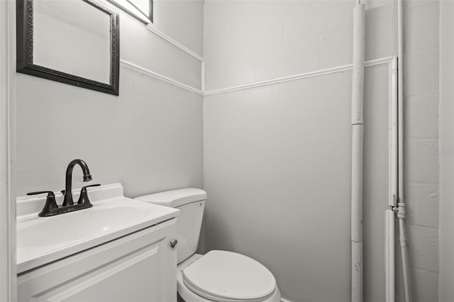 bathroom with concrete block wall, toilet, and vanity