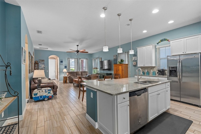 kitchen with appliances with stainless steel finishes, arched walkways, white cabinetry, a ceiling fan, and a sink