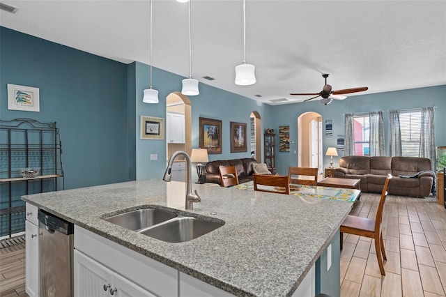 kitchen featuring open floor plan, dishwasher, pendant lighting, arched walkways, and a sink