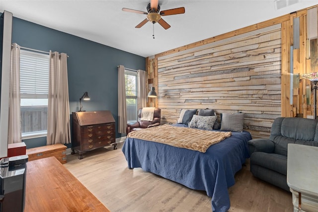 bedroom featuring visible vents, wooden walls, an accent wall, ceiling fan, and light wood-type flooring