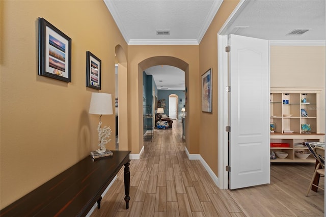 corridor with visible vents, light wood-style flooring, ornamental molding, a textured ceiling, and arched walkways