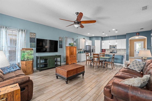 living area with visible vents, baseboards, arched walkways, ceiling fan, and light wood-style floors