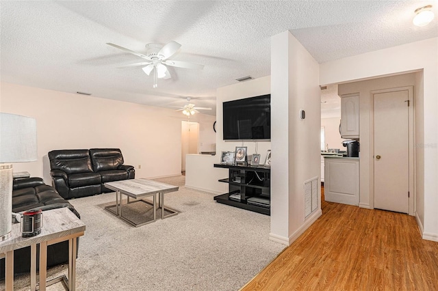 living area featuring visible vents, light wood-style floors, ceiling fan, and a textured ceiling