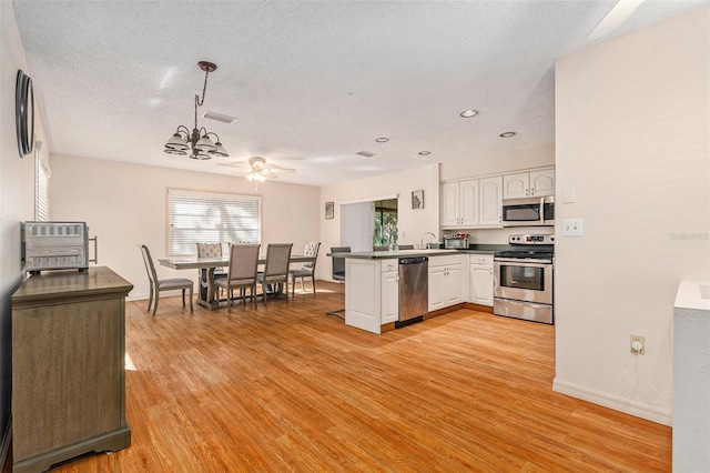 kitchen with dark countertops, appliances with stainless steel finishes, a peninsula, light wood-style floors, and white cabinets