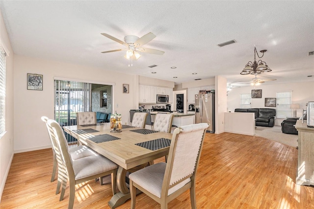 dining area featuring a textured ceiling, light wood-type flooring, visible vents, and ceiling fan