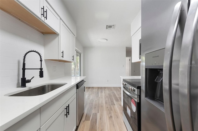 kitchen with visible vents, light wood-style flooring, a sink, decorative backsplash, and appliances with stainless steel finishes