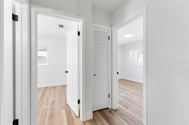 hall with light wood-type flooring, baseboards, and visible vents