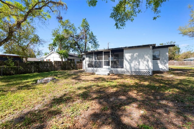 rear view of house featuring fence, a lawn, and a sunroom