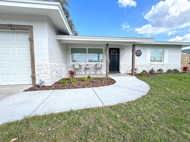 view of exterior entry featuring a garage, a lawn, covered porch, and concrete block siding