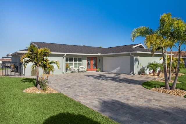 view of front of house featuring a front yard, stucco siding, french doors, decorative driveway, and an attached garage