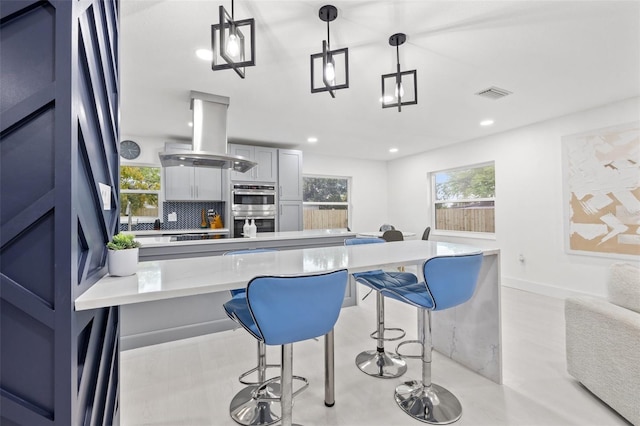 kitchen with visible vents, backsplash, a kitchen breakfast bar, island exhaust hood, and stainless steel double oven