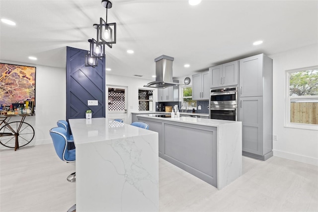 kitchen featuring a kitchen island, double oven, a barn door, decorative backsplash, and island exhaust hood