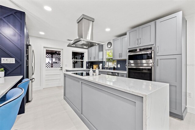 kitchen with tasteful backsplash, light stone countertops, recessed lighting, appliances with stainless steel finishes, and island exhaust hood