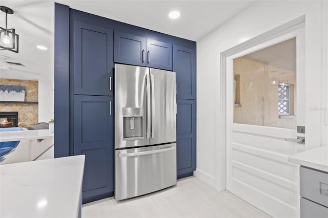 kitchen featuring blue cabinetry, light countertops, recessed lighting, a fireplace, and stainless steel fridge