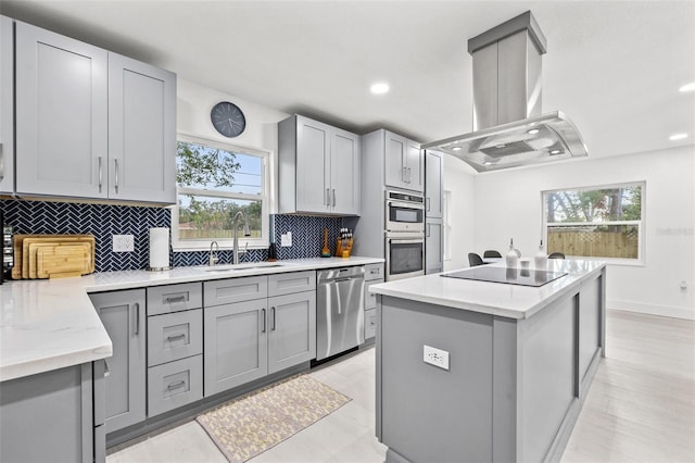 kitchen with gray cabinets, island exhaust hood, a sink, a center island, and appliances with stainless steel finishes