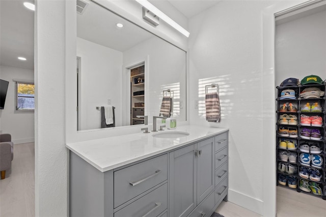 bathroom with visible vents, vanity, a walk in closet, and baseboards